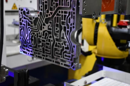 Machined automotive valve body held by a robot gripper at the inspection station